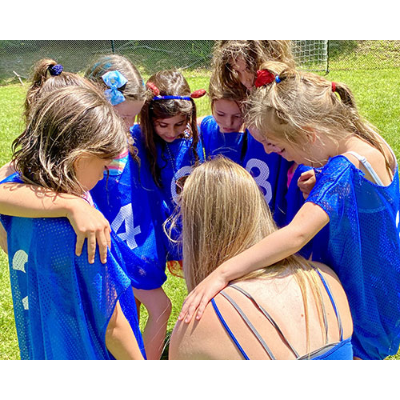 Motivating a girls soccer team with her back to the camera as a sport specialist at summer camp Ramaquois