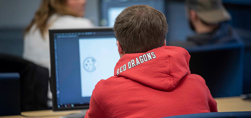 A student wearing a red dragon hoodie working at a compter