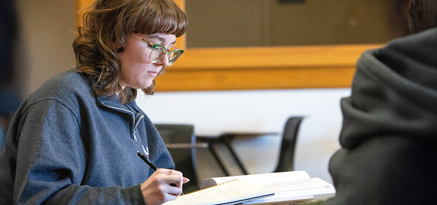 Student reading a book with a pen in hand