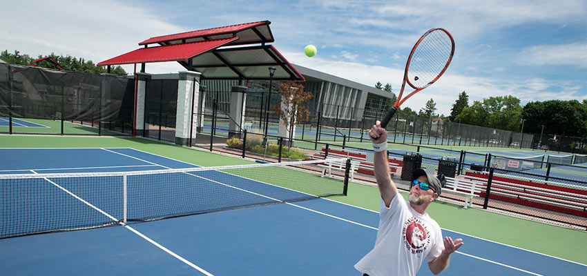 Person plays tennis on the courts outside of the Student Life Center