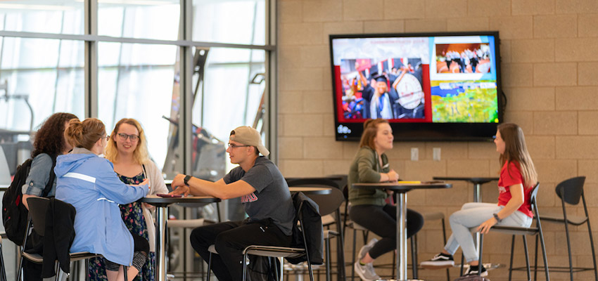 Students talking in front of a visual messaging system screen