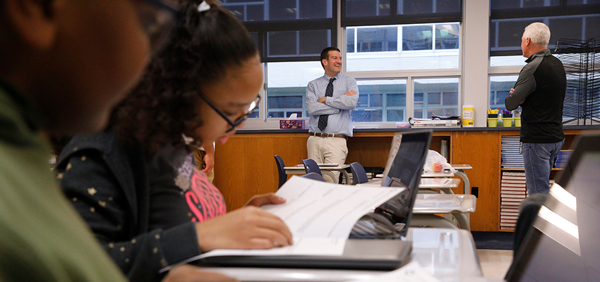 Two teachers talk while students do work in a high school classroom