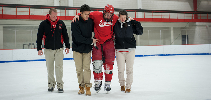Athletic training students getting hands-on experience assisting an injured hockey player off the ice
