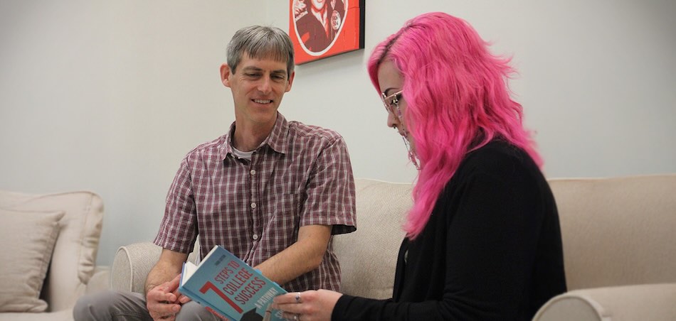 Two smiling disability resources office professionals seated at a couch, reviewing a book titled 7 Steps to College Success