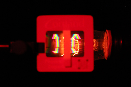 photo of a grating with a thin strip of paper across the center to block the direct light from the filament of a bulb 
