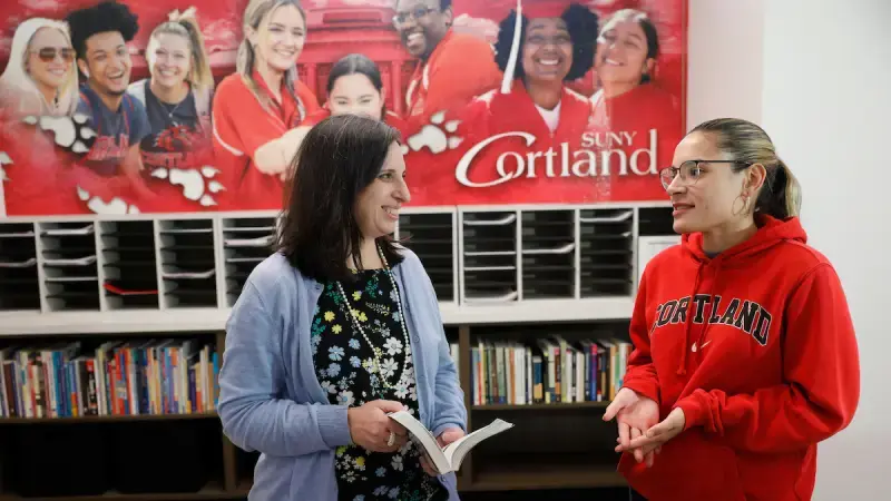 Director and student talking in from of Cortland banner