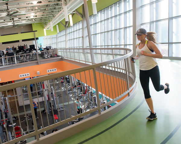Student running the track at the Student Life Center with weight and cardio machines in the background