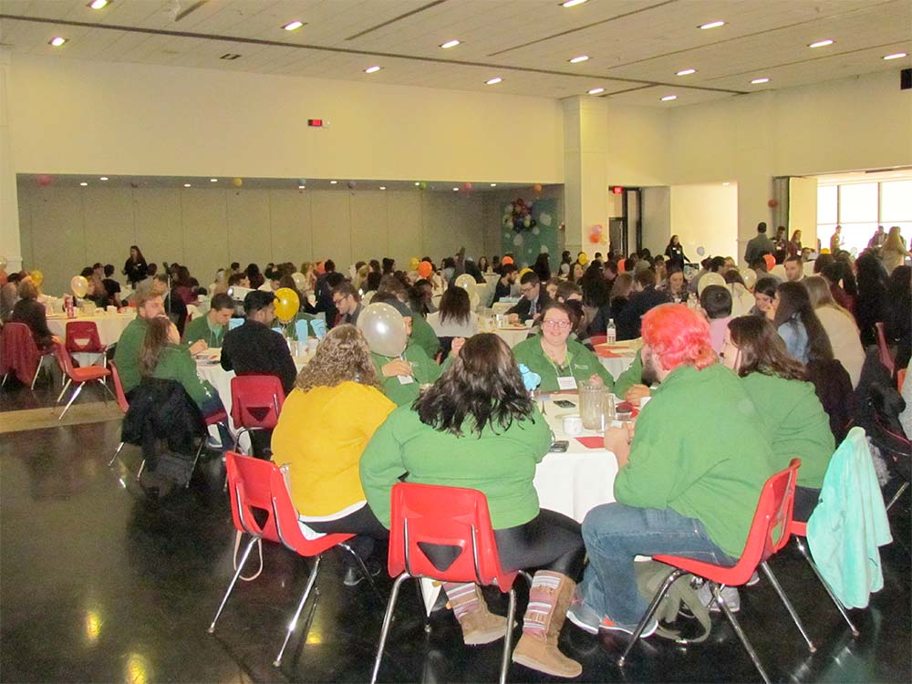 A large room full of conference attendees sit together at tables